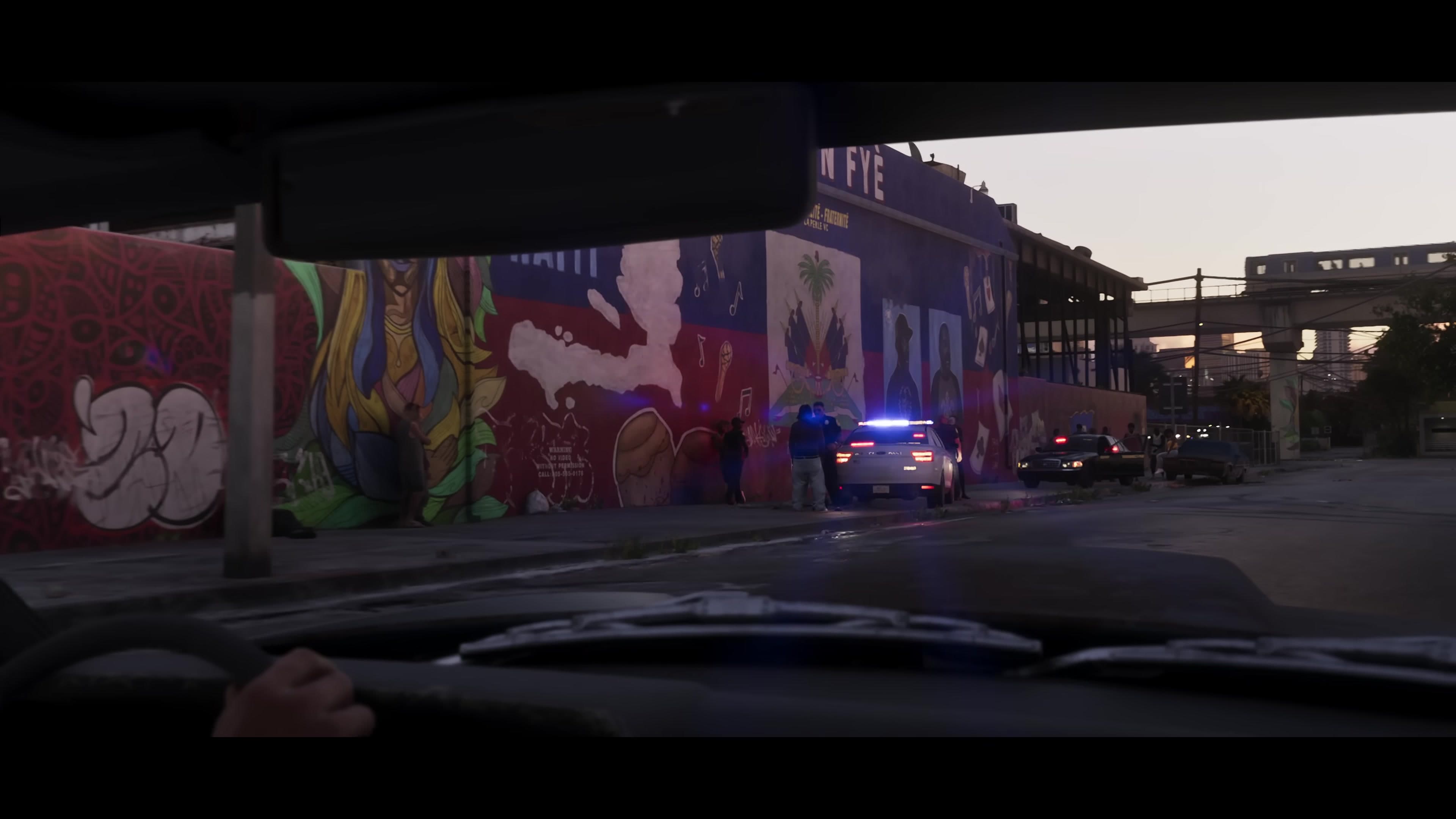 Police arrest scene in front of a mural, seen from inside a car
